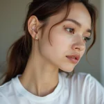 Jeune femme montrant plusieurs piercings d'oreille dont un helix, un lobe et un tragus avec des bijoux dorés minimalistes